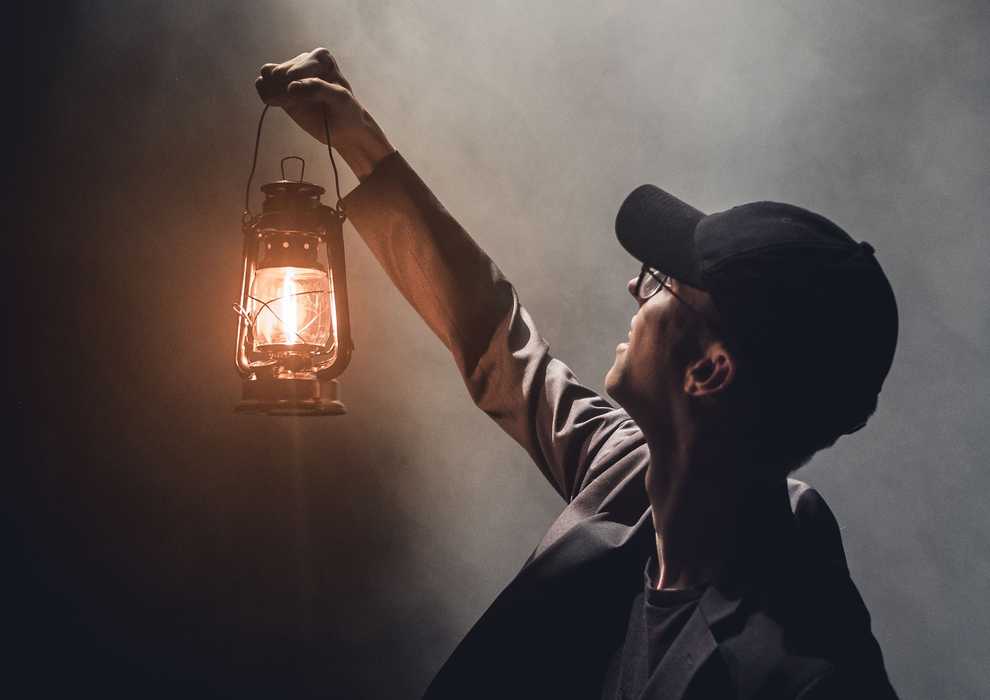 Man holding a lantern in the dark towards where the daylight come from